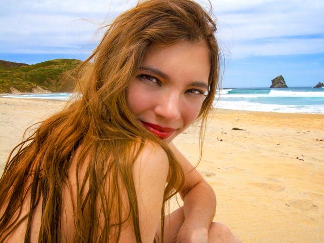 Sunbathing skinny dipping woman with beautiful face and red lips enjoying vacation on the perfect golden sandy beach in New Zealand, looking over the shoulder and smiling