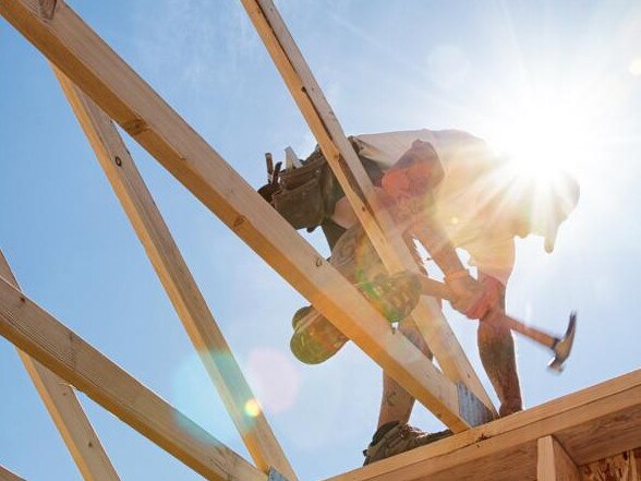 Construction worker framing a building against a sunny blue sky.