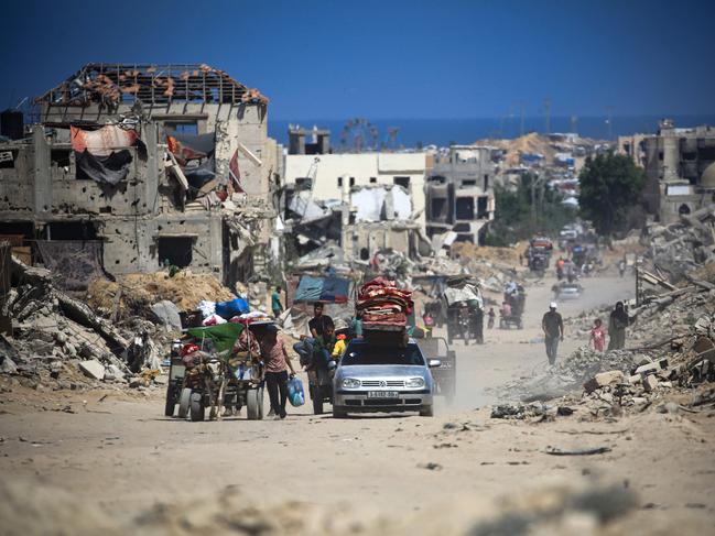 TOPSHOT - Palestinians walk and drive past buildings destroyed during previous Israeli bombardment, in Khan Yunis in the southern Gaza Strip on July 3, 2024, amid the ongoing conflict between Israel and the Palestinian Hamas militant group. (Photo by Eyad BABA / AFP)