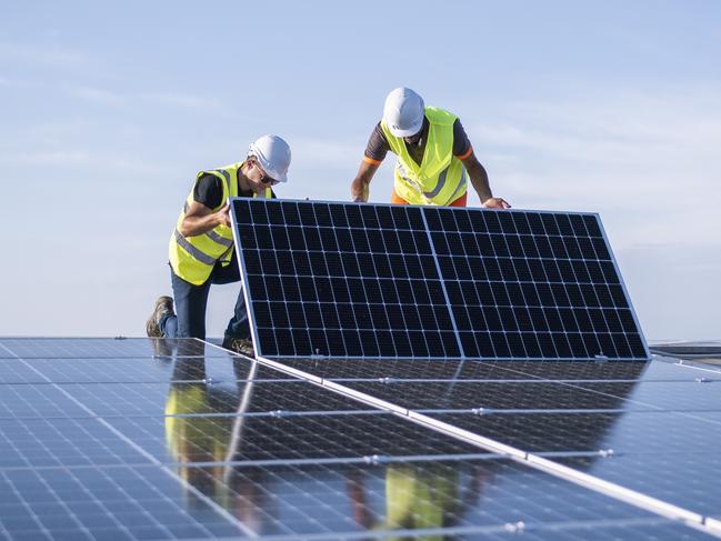 Team of two engineers installing solar panels on industrial factory roof.