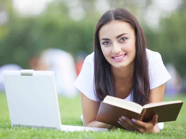 Brunette girl with notebook and book on green grass in the park. To illustrate online study. iStock image