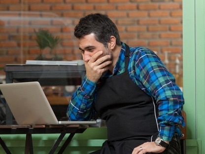 RendezView. Cafe owner sitting at table on computer looking stressed. (Pic: iStock)