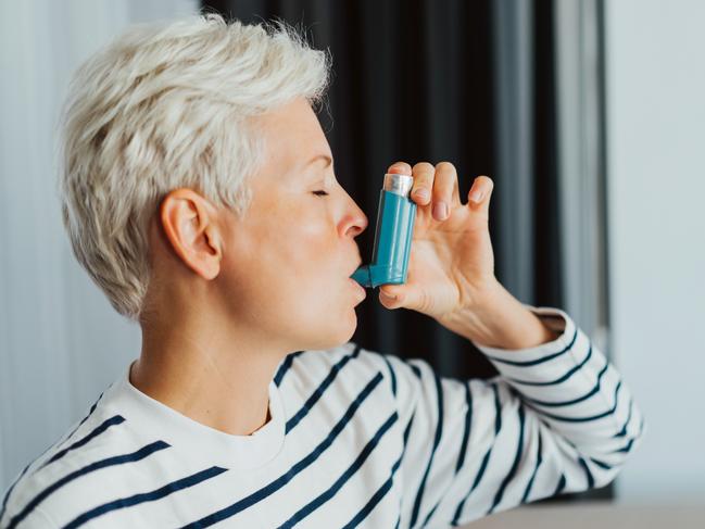 Woman using an asthma inhaler indoors. Using medication during an asthma attack