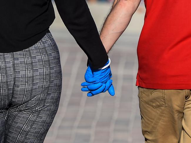 A couple holds hands while wearing gloves as they walks in South Beach, Miami, amid fears over the spread of the novel coronavirus (COVID-19) on April 1, 2020. - Americans were told on March 31 to brace for "very painful" weeks ahead in a worsening coronavirus pandemic projected to claim up to a quarter million US lives, as fatalities spiked in European hotspots Spain, France and Britain. (Photo by CHANDAN KHANNA / AFP)