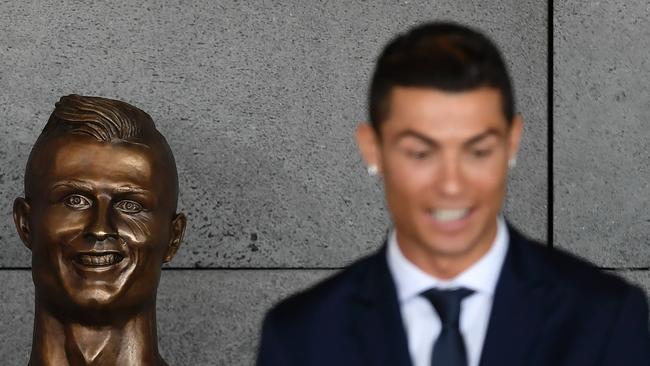 Portuguese footballer Cristiano Ronaldo stands beside a bust.