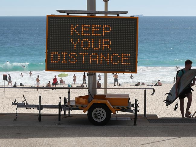 PERTH, AUSTRALIA - APRIL 10: A surfer walks back from the beach past social distancing signage at Scarborough Beach on April 10, 2020 in Perth, Australia. Australians have been urged to avoid all unnecessary travel over the Easter long weekend as the nation continues to deal with the COVID-19 pandemic. The Federal Government has closed all non-essential business and implemented strict social distancing rules, while public gatherings are now limited to two people. New South Wales and Victoria have also enacted additional lockdown measures to allow police the power to fine people who breach the two-person outdoor gathering limit or leave their homes without a reasonable excuse. Queensland, Western Australia, South Australia, Tasmania and the Northern Territory have all closed their borders to non-essential travellers and international arrivals into Australia are being sent to mandatory quarantine in hotels for 14 days. (Photo by Paul Kane/Getty Images)