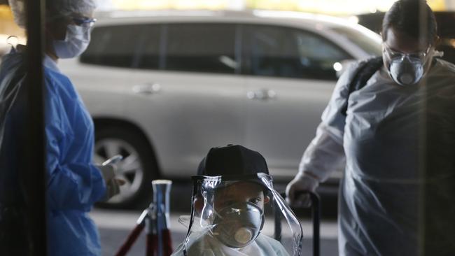 Wearing a face shield and face mask, a boy and his aunt, right, pass a temperature check point on Paraguay for a flight to Miami, Florida. Picture: AP