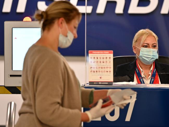 An airport worker serves a passenger behind plexiglas. Picture: AFP