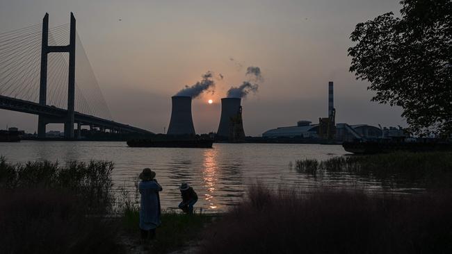 A couple take pictures along the Huangpu river across the Wujing Coal-Electricity Power Station in Shanghai. China’s coal-hungry heavy industry is already facing restricted hours due to lack of supply. Picture: AFP