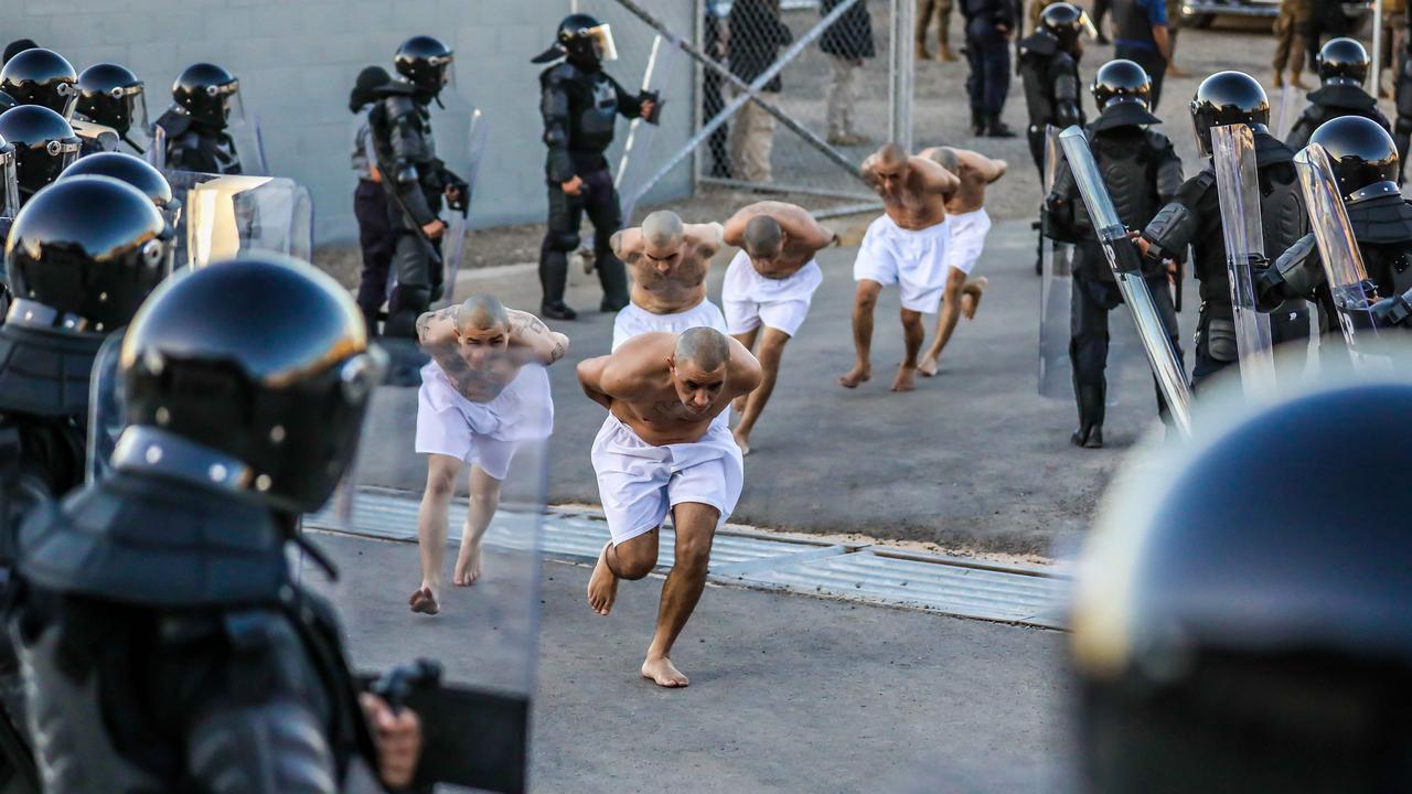 Police officers keep watch during the arrival of inmates. (Photo by Salvadorean Presidency / AFP)