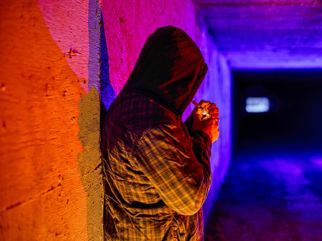 Criminal Drug Addict Smoking Drugs in Underground Tunnel - Man smoking drugs out of glass pipe in underground urban setting. Poverty, crime and homeless drug addiction theme.