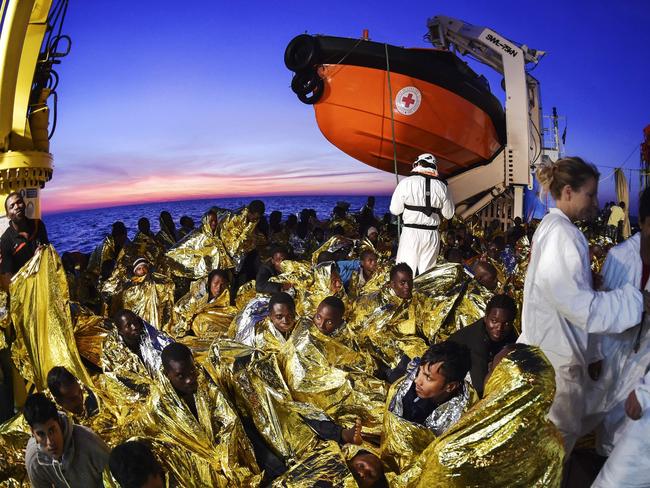 Migrants and refugees wrapped in survival foil blankets rest next to rescue members aboard the Topaz Responder ship run by Maltese NGO Moas and the Italian Red Cross after a rescue operation, early morning on November 5, 2016 off the coast of Libya. / AFP PHOTO / ANDREAS SOLARO