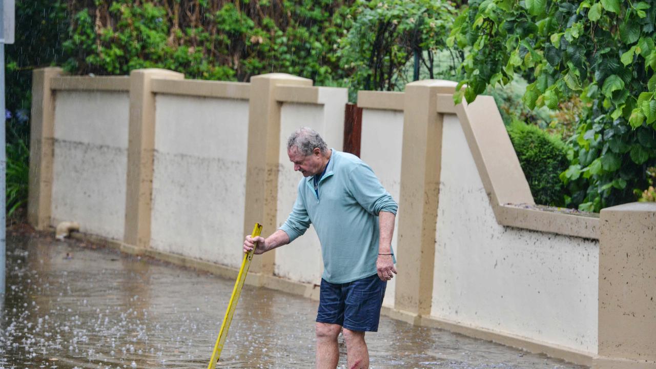 A Wayville resident tries to clear his drains. The mark on the wall shows how high the floodwaters rose. Picture: Brenton Edwards