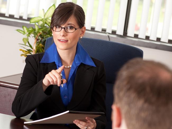 CAREERS: Color stock photo of a young businesswoman sitting in an office at a desk lecturing or questioning a young businessman.