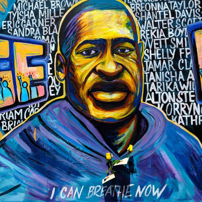 Two yellow roses are pinned to a mural of George Floyd bearing the words 