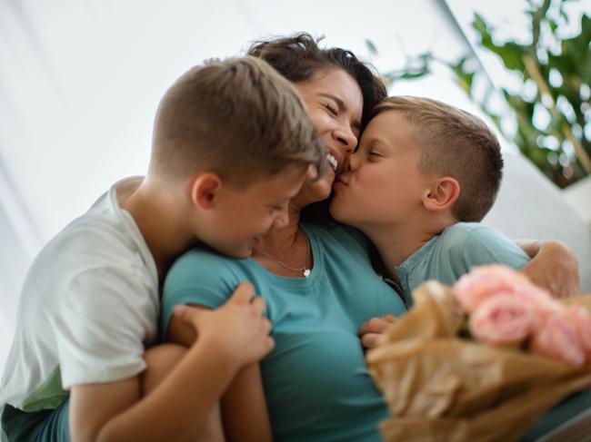 Sons hugging and kissing their mother and giving her a bouquet of roses for Mother's Day.