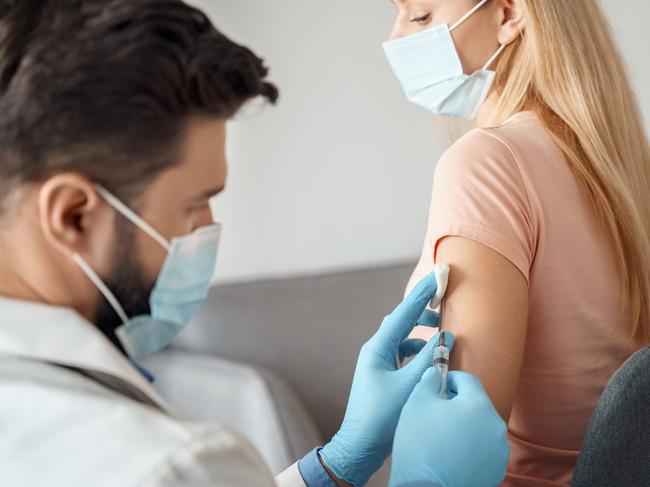 Young caucasian woman in medical mask getting injection covid19 coronavirus flu vaccine from doctor in protective respirator and gloves holding syringe. Antiviral immunization campaign during pandemic