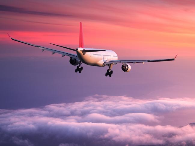 ESCAPE. FLYING HACKS. 23 SEPTEMBER 2018.  Airplane. Landscape with big white passenger airplane is flying in the red sky over the clouds at colorful sunset. Journey. Passenger airliner is landing at dusk. Business trip. Commercial plane Picture: istock