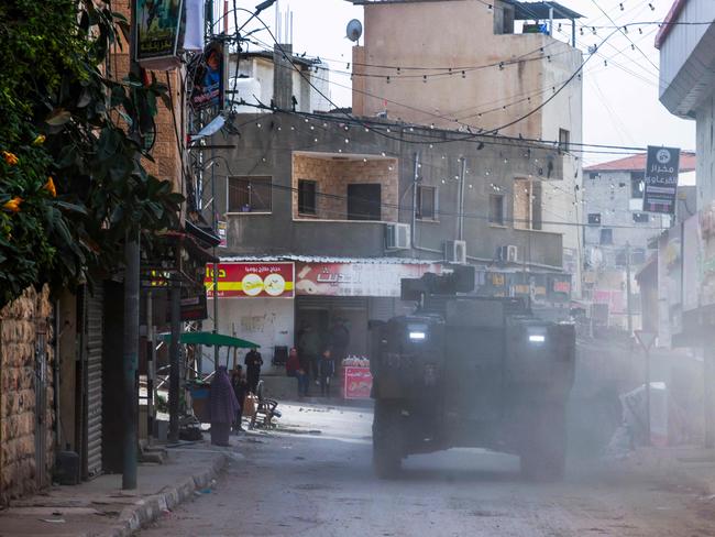 Palestinian shopkeepers look as Israeli armoured vehicles drive by during a raid in the eastern neighbourhood of Jenin. Picture: AFP