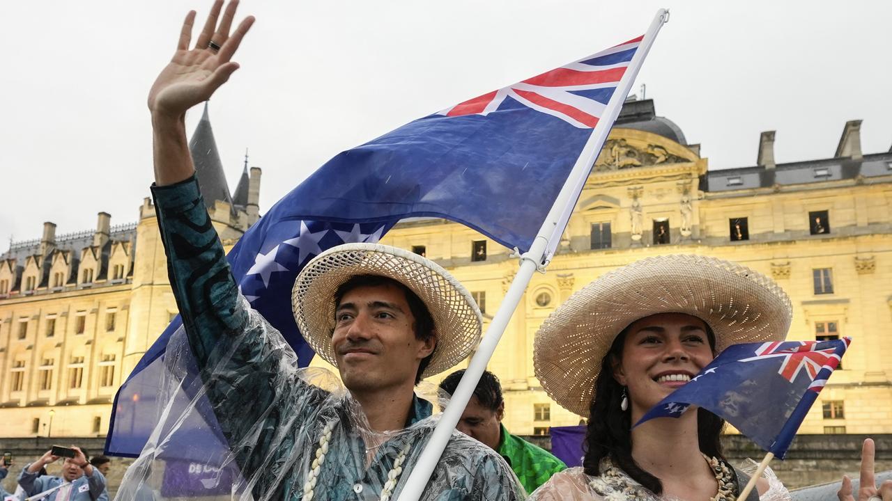 FRANCE - JULY 26: Alex Beddoes and Lanihei Connolly of the Cook Islands delegation wave their national flag on a boat on the River Seine during the opening ceremony of the Paris 2024 Olympic Games on July 26, 2024 in Paris, France. (Photo by Lee Jin-man - Pool/Getty Images)