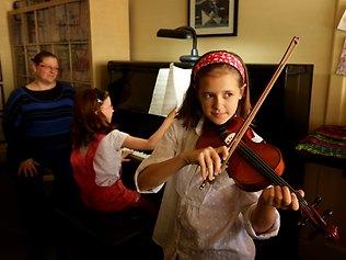 Music teacher Katie Eury watches her daughter Charlotte, on piano, and violin student Tarlisha Simpson-Clayton perform. Picture: Stuart McEvoy