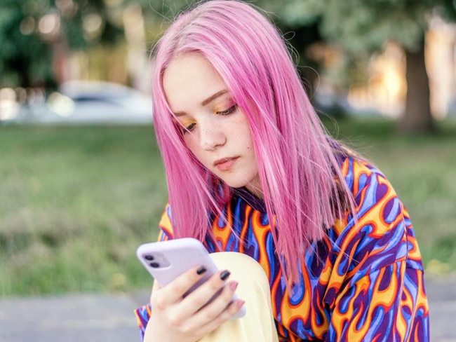 Pink-haired teenage hipster girl in a colorful bright T-shirt is using a smartphone on a summer day.Summer concept.Generation Z style.Social media concept.