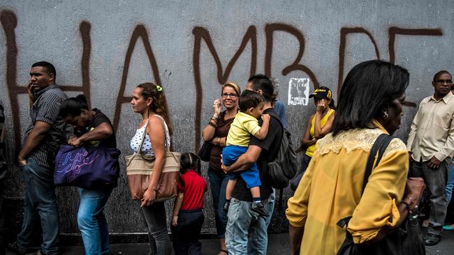 People queue next to a wall with a graffiti reading “Hunger” in Caracas. Picture: Juan Barreto/AFP
