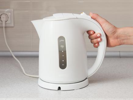 Electric Kettle in hand on the background of the kitchen.