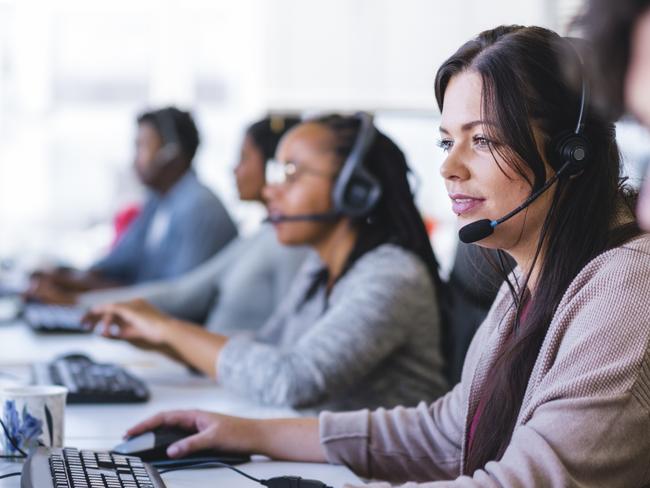 Young businesswoman wearing headset while using computer. Row of operators are sitting at desk. They are working in call center.