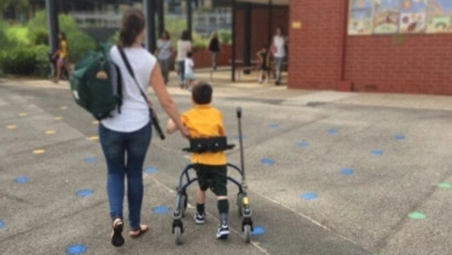 A boy and his mother walk into their local primary school for the first day of school.