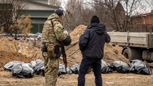 A member of the Ukrainian army and a policeman stand near body bags exhumed from a mass grave where civilians where buried in Bucha, on the outskirts of Kyiv, on April 13.