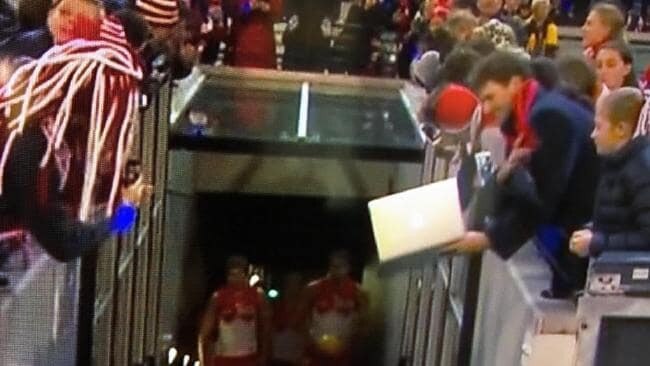 One fan uses a laptop to take a photo of the Sydney Swans running onto the ground.