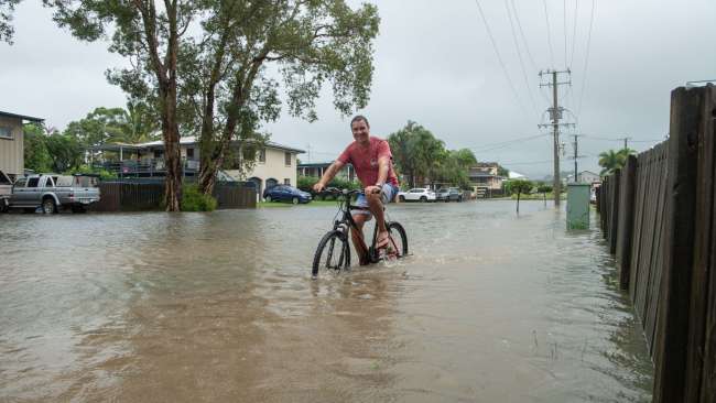 Maroochydore resident Jamie Moore rides to the shops as the Maroochy River rises on Saturday. Picture: Brad Fleet