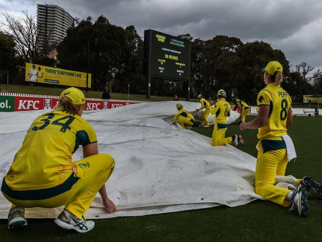 MELBOURNE, AUSTRALIA - OCTOBER 12: Australian players assist ground staff in carrying the pitch covers as the rain comes in during game two of the womens One Day International series between Australia and the West Indies at Junction Oval on October 12, 2023 in Melbourne, Australia. (Photo by Asanka Ratnayake/Getty Images)