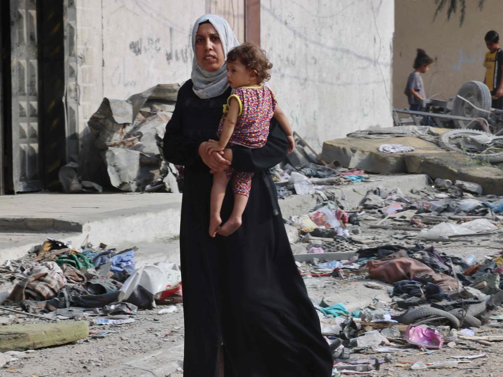 A Palestinian woman carries a child walks through debris in a residential neighbourhood in Rafah after Israeli air strikes. Picture: Said Khatib/AFP