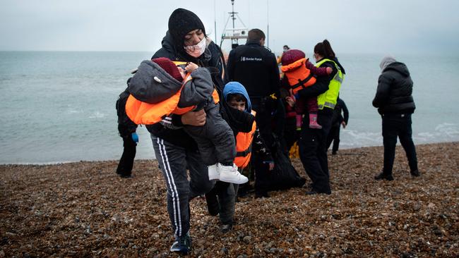 A migrant carries her children after being helped ashore at Dungeness on the southeast coast of England. Picture: AFP.