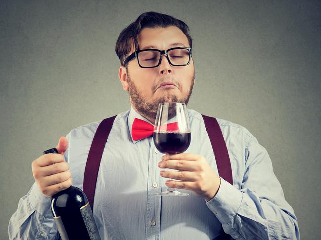 Concentrated man holding bottle of wine and smelling beverage with eyes closed on gray backdrop.