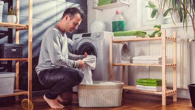 Man wearing grey sweater putting clothes into washing machine at laundry room