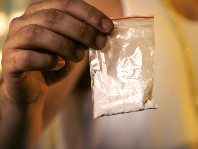 Brutal Drug Dealer Wearing Sleeveless Shirt and Gold Chain Holds and Offers Sample Bag Full of Drugs. He Lives in the Abandoned Building with Boarded Up Windows.