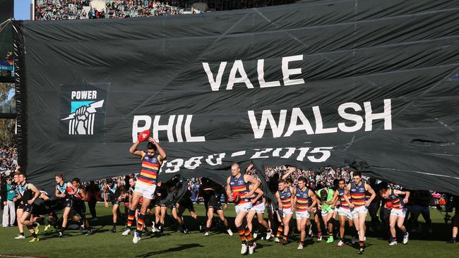 Adelaide and Port Adelaide players run through the joint Phil Walsh tribute banner at Adelaide Oval in 2015. Picture: AAP Image/Ben Macmahon