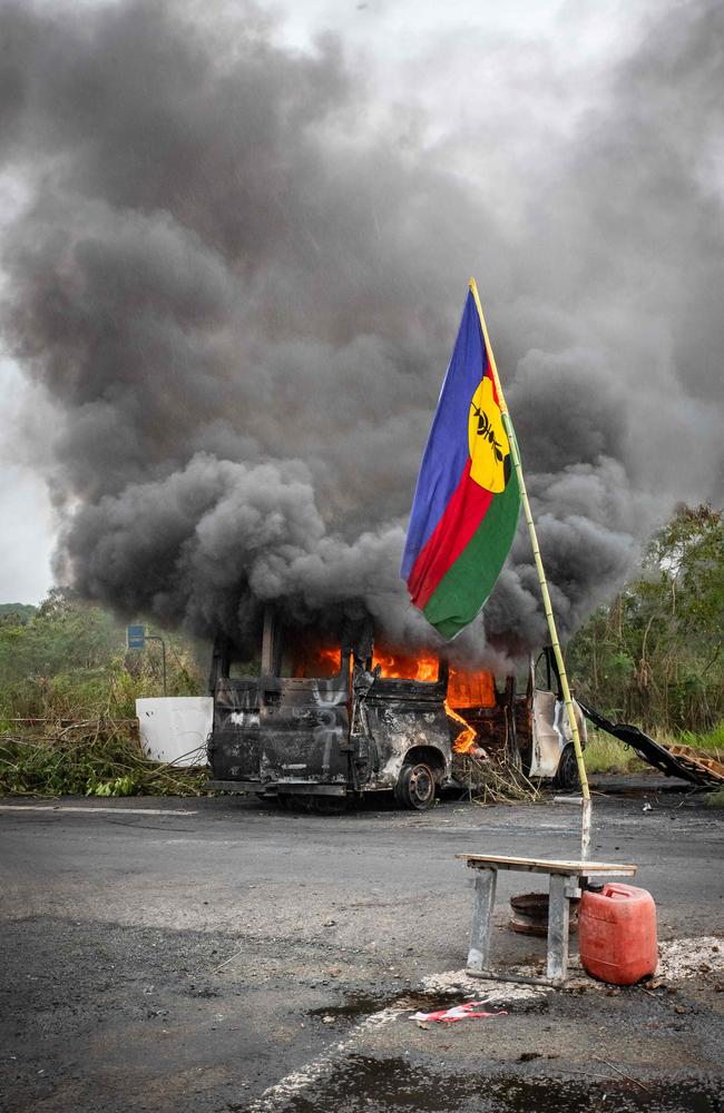 A Kanak flag waving next to a burning vehicle at an independantist roadblock at La Tamoa, in the commune of Paita, New Caledonia. Picture: Delphine Mayeur/AFP