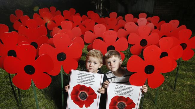 Felix, 4, and Oscar, 6, hold the Herald Sun Poppy Poster with the poppies they made with their parents Mark and Sarah Algie in the garage for family and friends. Picture: David Caird