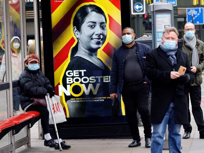 People wait at a bus stop displaying a government advertisement promoting the NHS Covid-19 vaccine Booster program in London. Picture: AFP