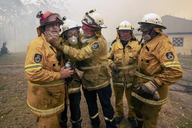 RFS captain John Sharpe (red helmet) was overcome with emotion as his colleagues helped him extinguish a blaze surrounding his home at Bawley Point. Picture: Gary Ramage