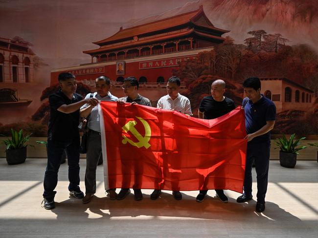 This photo taken on June 11, 2021 shows people with a flag of the Chinese Communist Party preparing to pose for a photo as they visit the museum of the First National Congress of the Chinese Communist Party in Shanghai. - As the ruling body celebrates its 100th birthday on July 1, current members describe an increasingly cult-like atmosphere under leader Xi Jinping, propagandising successes such as its control of the coronavirus, and viewed as the only viable saviour for China. (Photo by Hector RETAMAL / AFP) / TO GO WITH China-politics-party-anniversary-members,FOCUS by Dan Martin