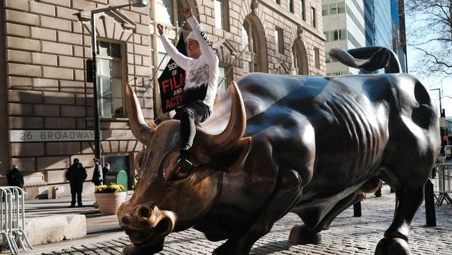 A wild ride for markets: a man sits on the Wall Street bull near the New York Stock Exchange. Picture: AFP