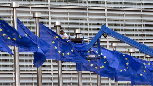 A worker on a lift adjusts the member flags in front of European Union headquarters in Brussels today. Picture: Virginia Mayo