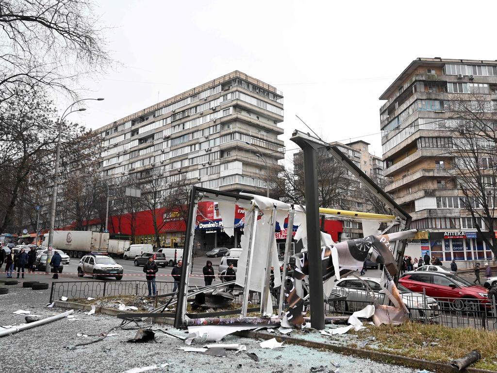 People are seen outside the cordoned-off area around the remains of a shell in a street in Kyiv on February 24, 2022 as invasion began. Picture: Sergei Supinsky / AFP