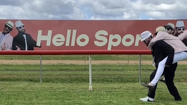 Hello Sport’s Tom and Eddy imitating a horse running down the main straight at the Dubbo Turf Club, in front of their new signage. Photo: Instagram