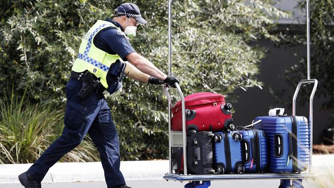 A Tasmania Police officer pushes luggage belonging to passengers who arrived on a Jestar flight from Melbourne who have been taken to the Travelodge Hotel in Cambridge for their mandatory two-week quarantine. Picture: ZAK SIMMONDS